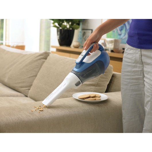 BLACKDECKER DV7210N handheld vacuum cleaner cleaning cookie crumbs from beige sofa in living room.