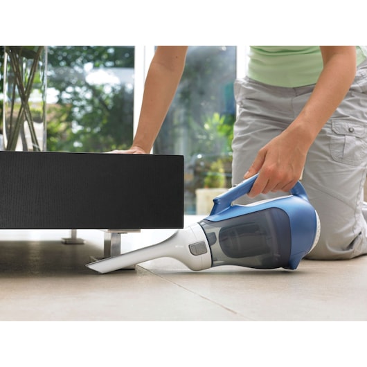 BLACKDECKER DV7210N handheld vacuum cleaner in blue and white, used to clean under furniture indoors.