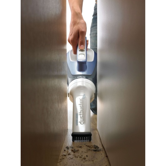 BLACKDECKER DV7210N handheld vacuum cleaning dust with brush attachment in a narrow space.
