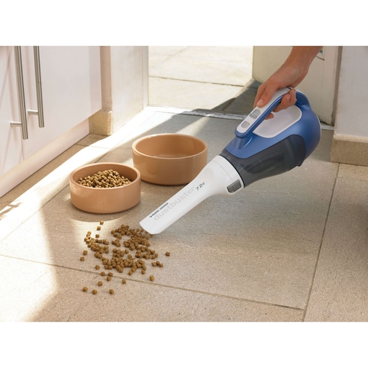 BLACKDECKER DV7210N handheld vacuum cleaning spilled pet food near bowls, side angle, indoor setting.