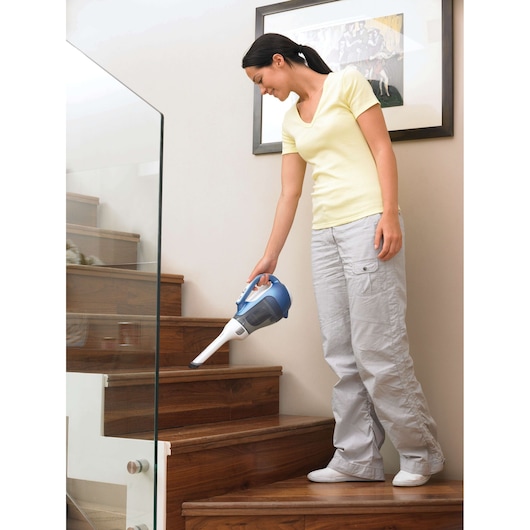 BLACKDECKER DV7210N handheld vacuum cleaner in use cleaning wooden stairs, indoor setting.