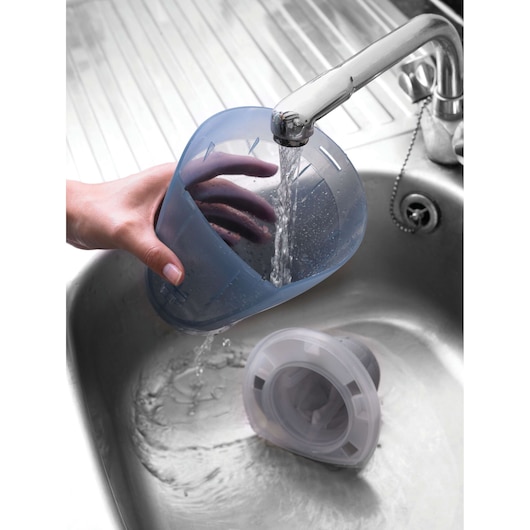 Photo of BLACKDECKER DV9610ECN dust container and filter being rinsed under running water in a kitchen sink.