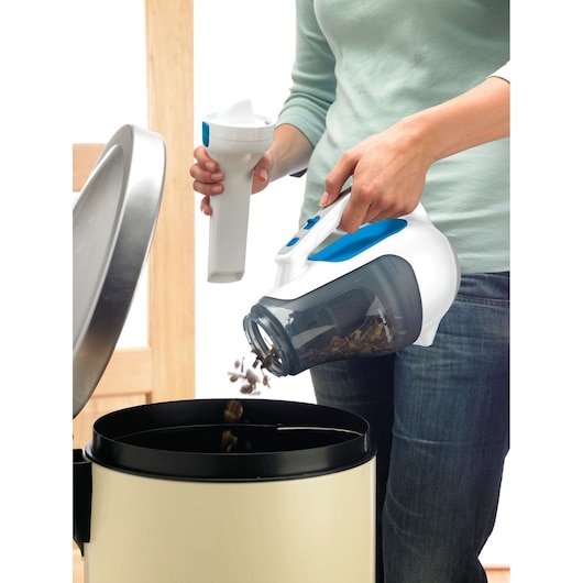BLACK+DECKER DV9610N handheld vacuum in use, dirt being emptied into a trash can, close-up.
