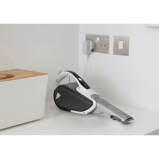 Photo of BLACKDECKER DVJ215J handheld vacuum cleaner in white and grey, charging on a countertop.