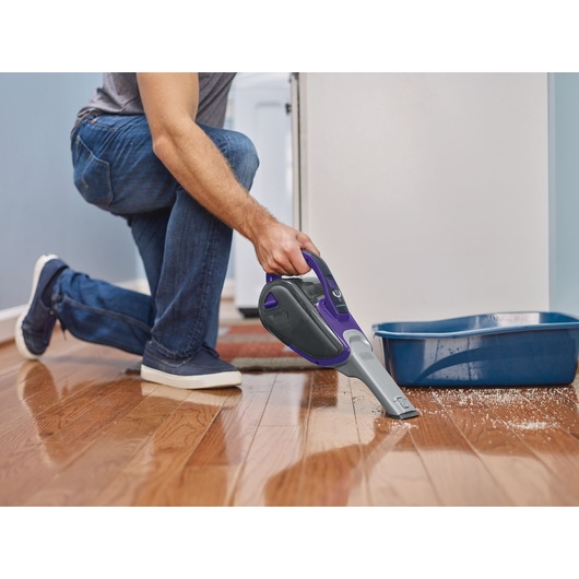 BLACKDECKER DVJ325BFSP handheld vacuum cleaning near a blue litter box on hardwood floor.