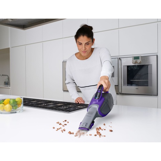 BLACKDECKER DVJ325BFSP handheld vacuum cleaning crumbs on kitchen counter, person using device.