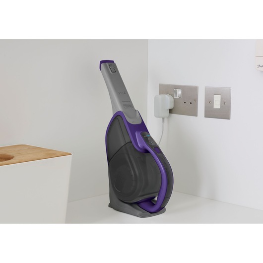 BLACKDECKER DVJ325BFSP cordless handheld vacuum in charging dock, grey and purple, on countertop.