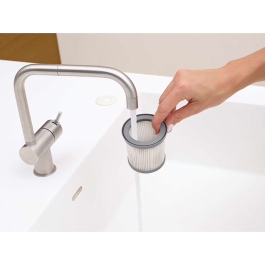 Photo of a person rinsing a BLACKDECKER DVJ325BFS vacuum filter under a modern kitchen faucet in a white sink.