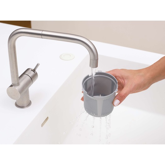 Photo of BLACKDECKER DVJ325BFS vacuum filter being washed under a stainless steel faucet in a white sink.