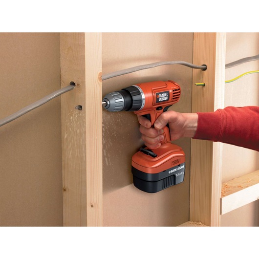 Photo of BLACKDECKER EPC14CA cordless drill in use, orange and black, drilling into wood framing indoors.