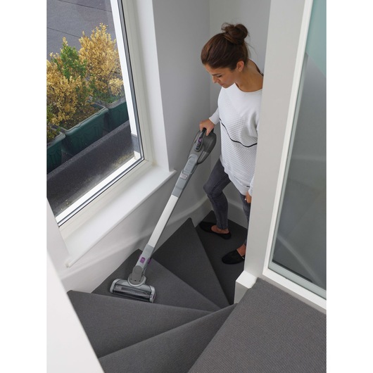 Photo of BLACKDECKER FEJ520JFS stick vacuum cleaning grey carpeted stairs indoors.
