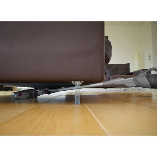 BLACKDECKER FEJ520JFS stick vacuum cleaning under brown sofa on wood floor, side angle.