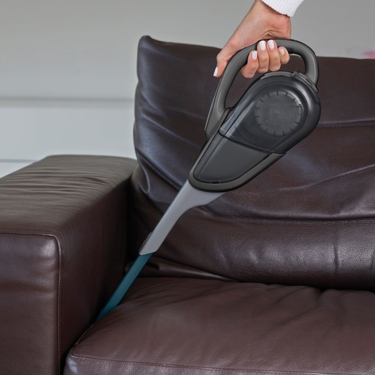 Photo of BLACKDECKER FEJ520JF handheld vacuum cleaning between brown leather sofa cushions.