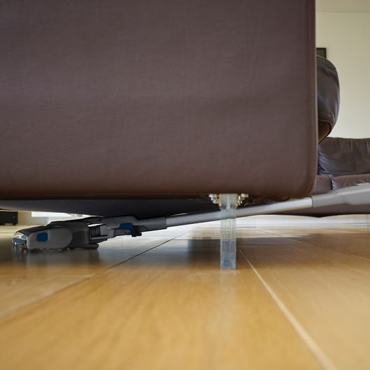 BLACKDECKER FEJ520JF cordless vacuum cleaning under brown sofa on wooden floor, side angle.
