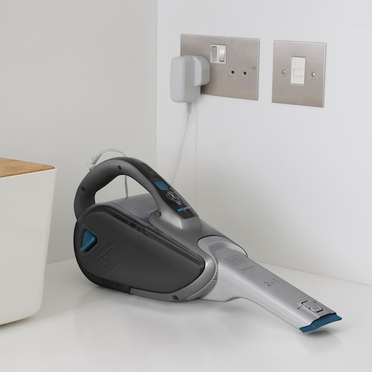 BLACK+DECKER FEJ520JF handheld cordless vacuum cleaner, grey and blue, lying on white surface near wall outlet.