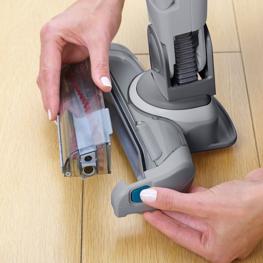 BLACKDECKER FEJ520JF cordless vacuum cleaner head close-up on light wood floor, hand removing brush roll.