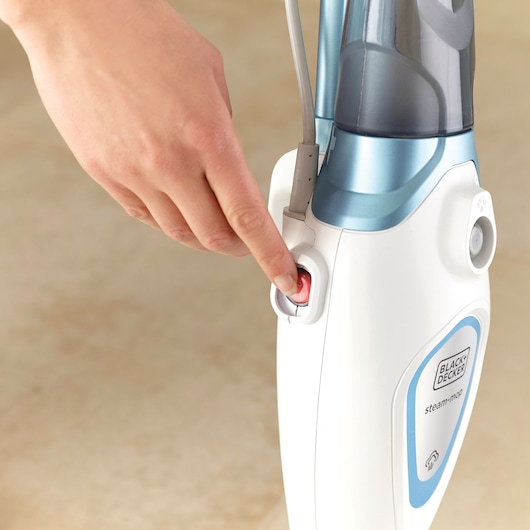 Close-up photo of hand pressing power button on BLACK+DECKER steam mop FSM1605, white and blue body.