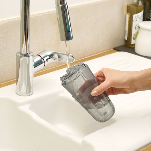 BLACKDECKER FSM1605 water tank being rinsed under a kitchen tap in a sink, close-up view.