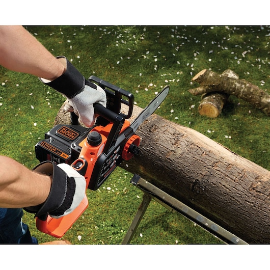 Photo of BLACK+DECKER GKC1825LB cordless chainsaw cutting log outdoors, orange and black design, gloved hands.