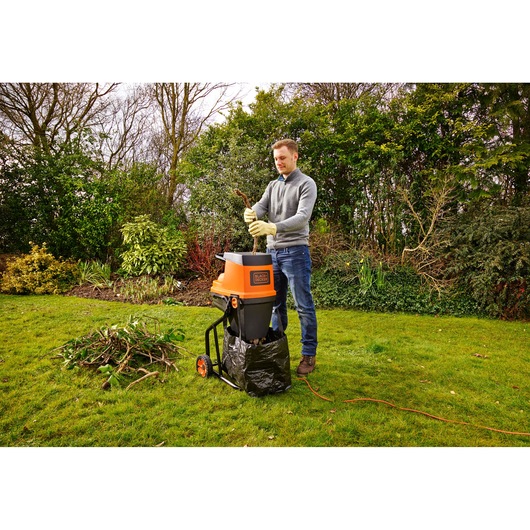 Man using BLACKDECKER GS2400 garden shredder in backyard, feeding branches into orange and black machine.