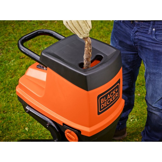 Photo of BLACK+DECKER GS2400 garden shredder, orange and black, with a gloved hand feeding a branch into the top.