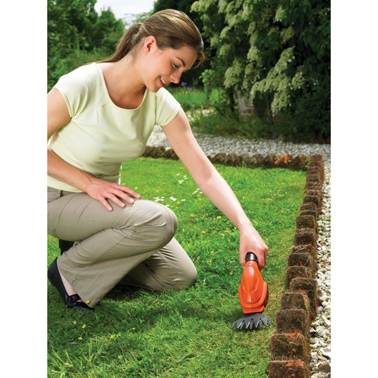 Photo of person kneeling in garden using BLACK+DECKER GSL200 grass shear along brick lawn edge.