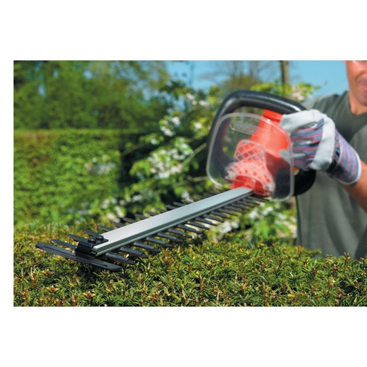 BLACKDECKER GT6030 hedge trimmer in use, close-up on blades trimming green hedge outdoors.