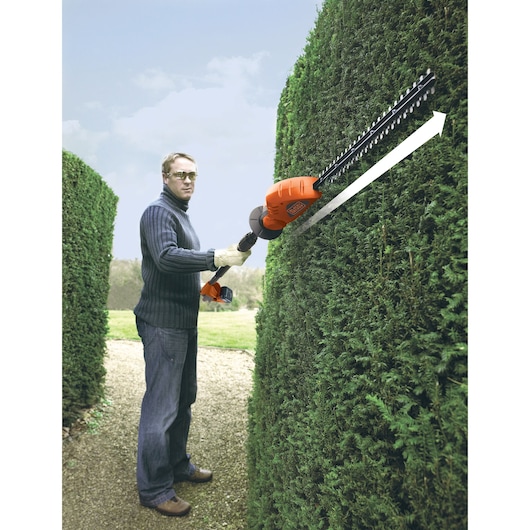 Photo of BLACK+DECKER GTC1843L hedge trimmer in use, trimming tall green hedge outdoors.