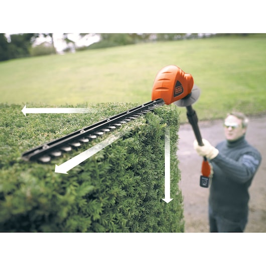 BLACKDECKER GTC1843L cordless hedge trimmer in use, trimming green hedge in outdoor setting.
