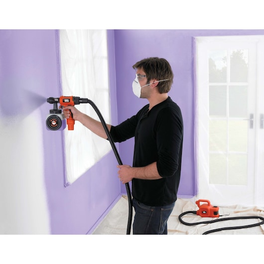 Photo of BLACKDECKER HVLP400 paint sprayer used on a purple wall, hose and base unit visible in home interior.