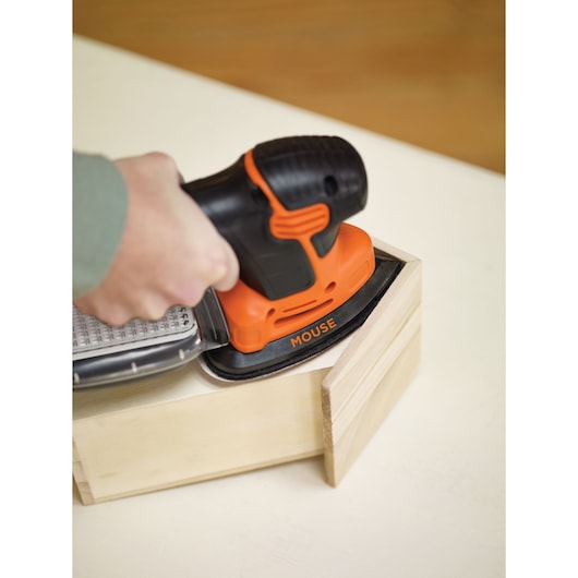BLACKDECKER KA2000 orange and black mouse sander in use on wooden box, closeup angle