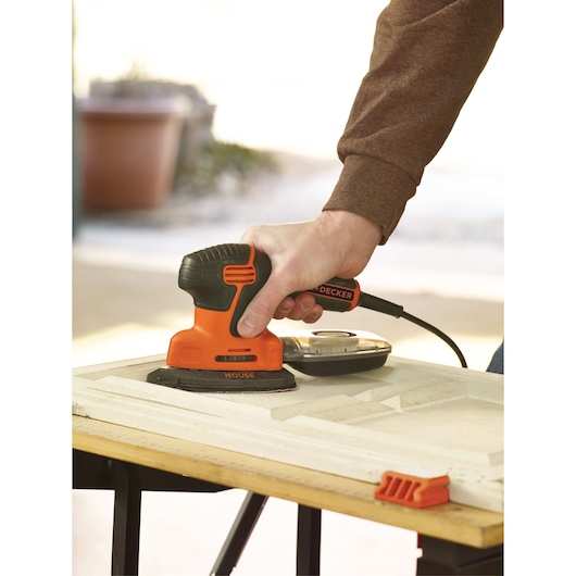 Person sanding wood with BLACKDECKER KA2000 orange and black detail sander, close-up view.