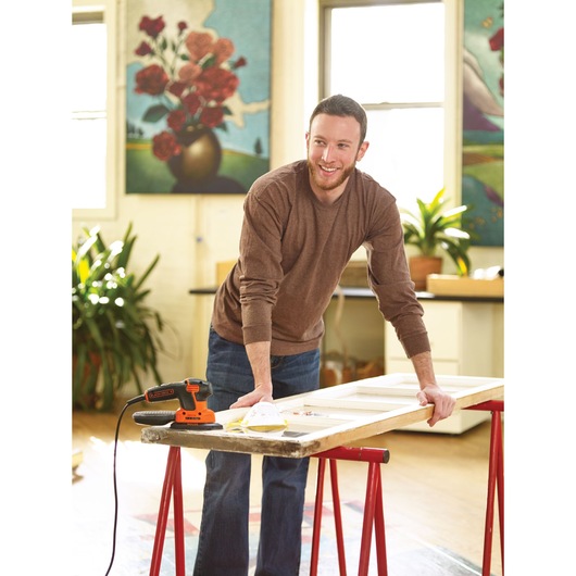 BLACKDECKER KA2000 detail sander on workbench next to person working on wooden frame in bright indoor space.