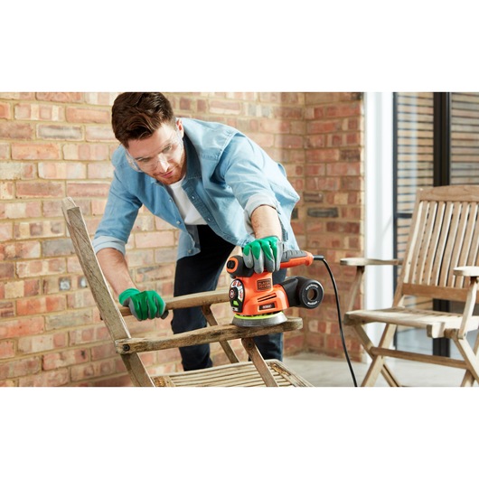 Photo of BLACKDECKER KA280 multi-sander being used to sand a wooden chair outdoors.