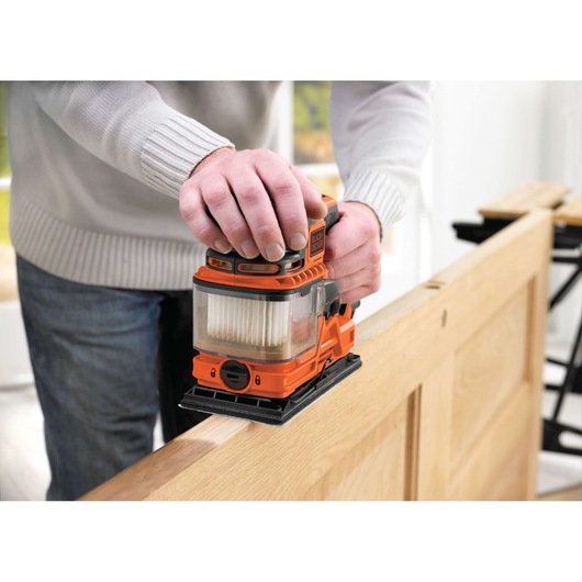 Photo of BLACK+DECKER KA330E orange finishing sander in use on a wooden door, close-up.