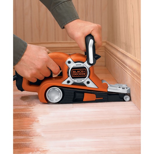 Photo of BLACKDECKER KA88 belt sander in use on a wooden floor near wall molding, close-up angle.