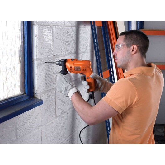 BLACKDECKER KR504RE orange corded drill held by person drilling into white brick wall.