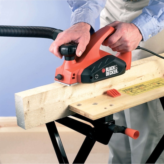 Photo of BLACKDECKER KW712KA electric planer used on wood, close-up side view, red and black tool in action.