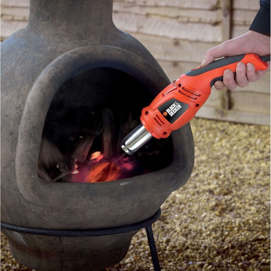 BLACKDECKER KX1692 heat gun igniting firewood inside outdoor fireplace, close-up photography.