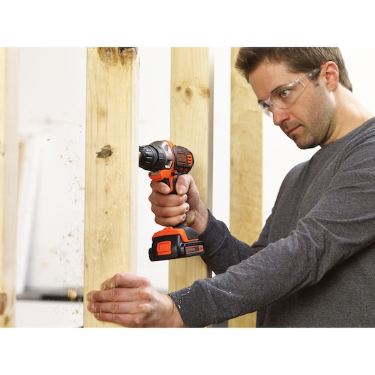 Photo of BLACKDECKER MT218K cordless drill in use, drilling through wood framing.