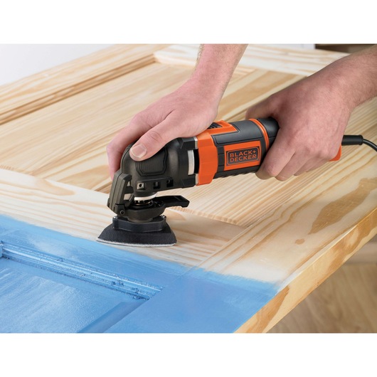 BLACK+DECKER MT300KA multi-tool sanding wood, handheld view, orange and black body.