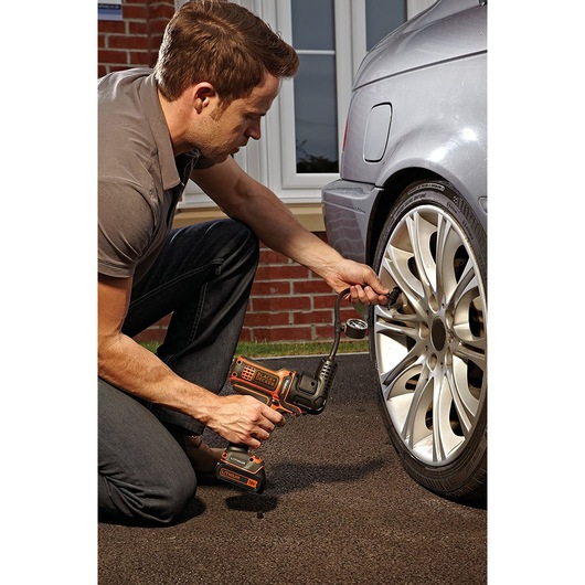 BLACKDECKER MTNF9 portable inflator in use on a car tire outdoors.