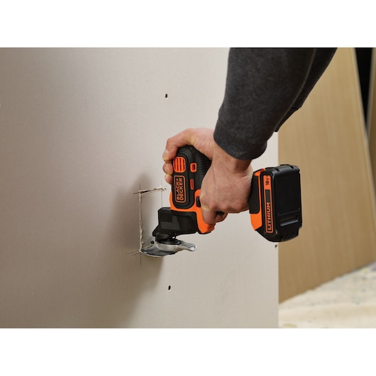 BLACKDECKER MTOS4 cordless multi-tool cutting drywall, close-up on hand and tool in use.