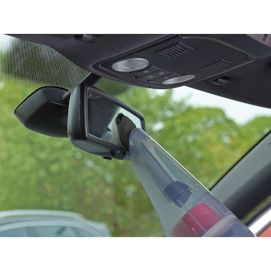 BLACKDECKER NV1210AV handheld vacuum cleaning car interior near rearview mirror, close-up angle.