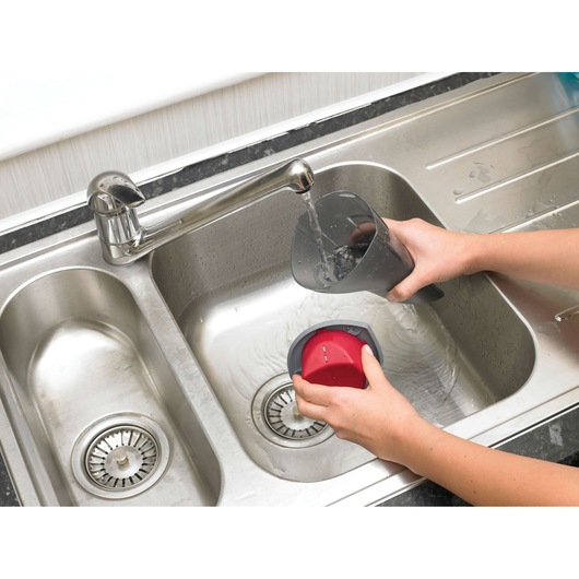 Photo of BLACKDECKER NV3620N vacuum dust container being cleaned under running water in a kitchen sink.