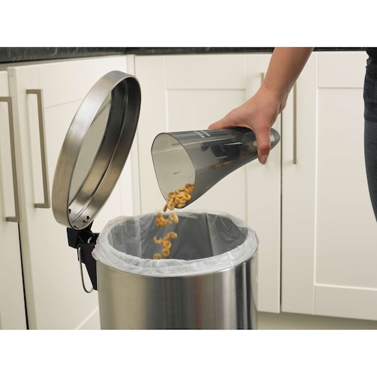 BLACKDECKER NV3620N vacuum dustbin being emptied into a stainless steel trash can in a kitchen.