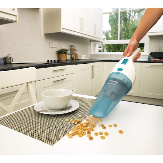 BLACKDECKER NW4820N handheld vacuum cleaning cereal from a white kitchen table, side angle.