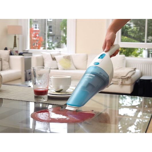 Photo of BLACK+DECKER NW4820N handheld vacuum cleaning liquid spill on glass table in a modern living room.