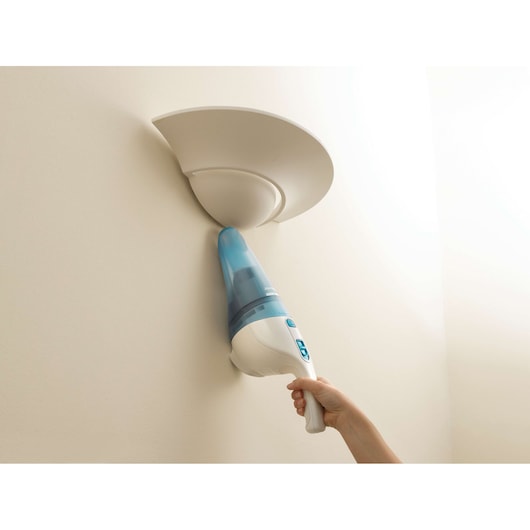 BLACK+DECKER NW4820N handheld vacuum with blue and white body cleaning around a wall light fixture, side angle.