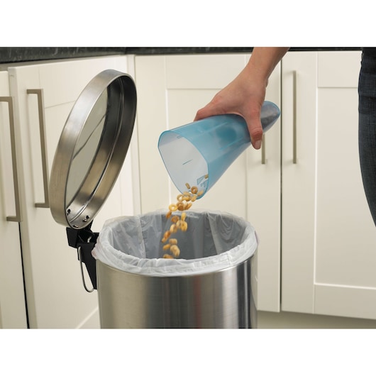 BLACKDECKER NW4820N vacuum dust container being emptied into a kitchen trash bin, side angle.